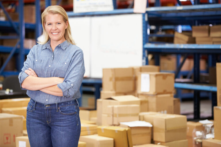 smiling female distribution warehouse manager standing near boxes