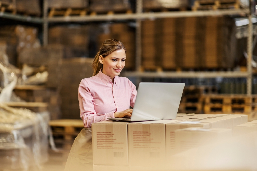 female convenience store distribution manager using inventory management software on laptop