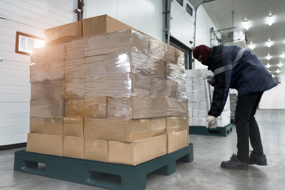 cold storage distribution warehouse worker wrapping pallet of goods