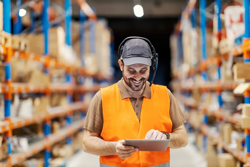 smiling man in warehouse using order picking headset and software on tablet