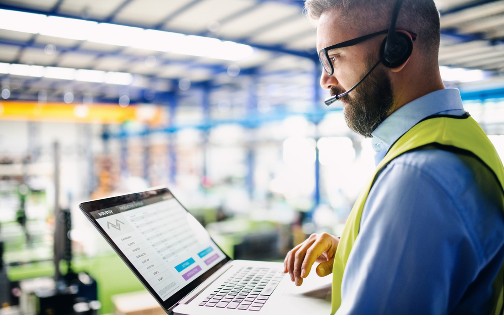 manager wearing headset setting up warehouse order picking technology with laptop